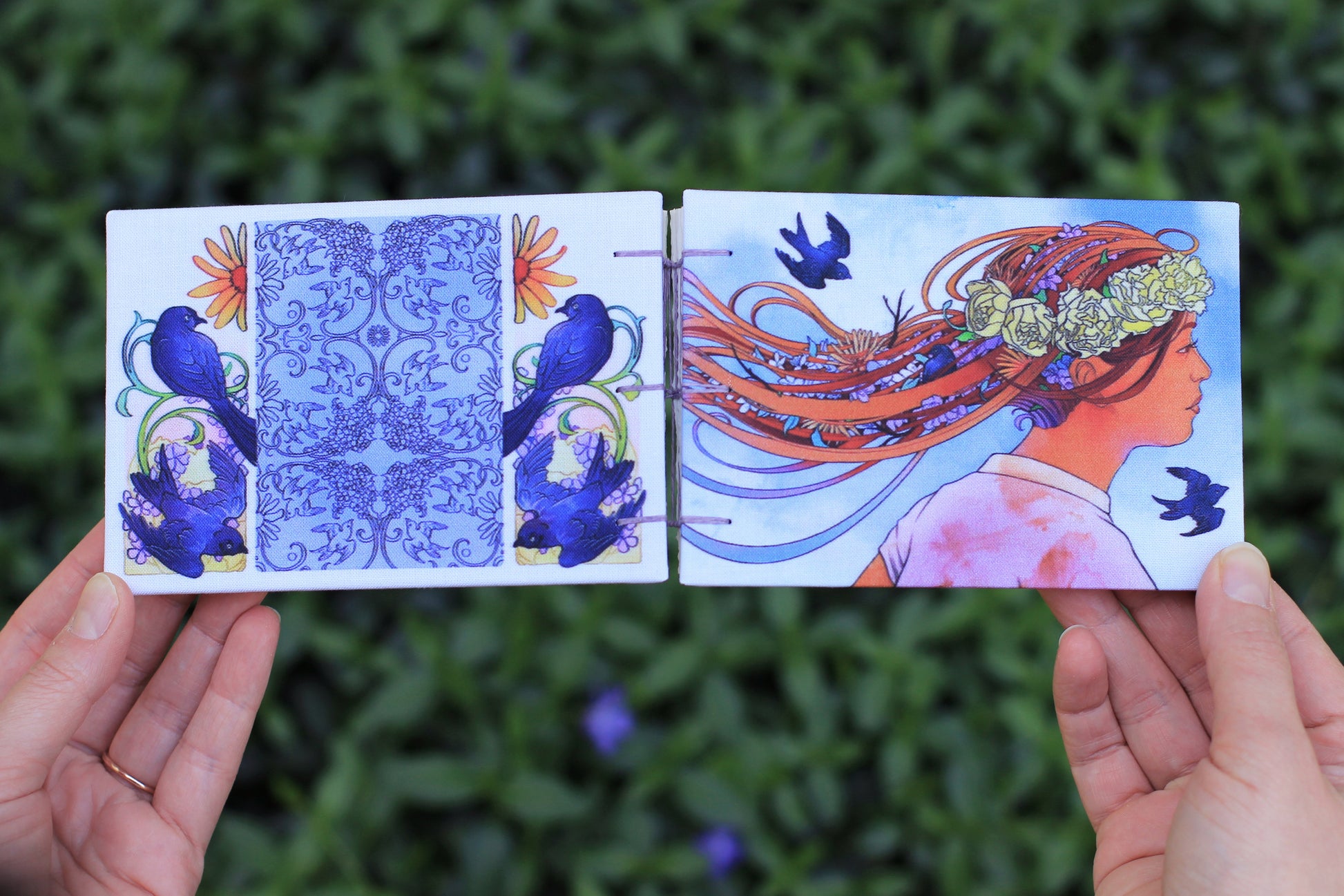 hand holding Emmylou Smith Lake Michigan Book Press sketchbook. Leafy green background.
