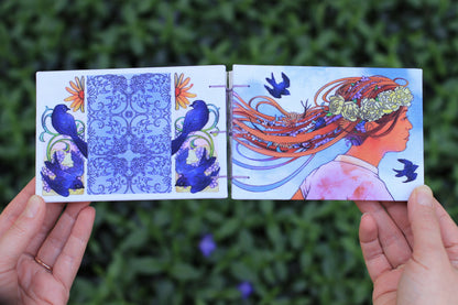 hand holding Emmylou Smith Lake Michigan Book Press sketchbook. Leafy green background.