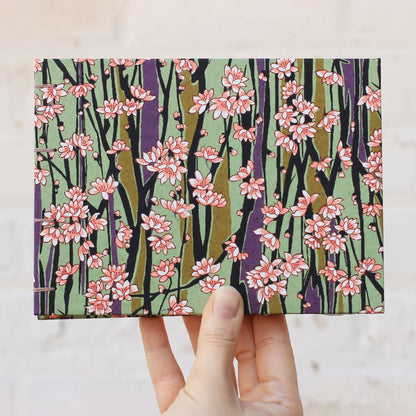 Hand holding a sketchbook with a floral pattern on the cover, photographed against white background.