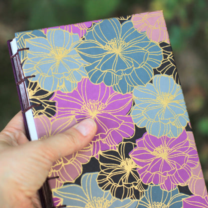 Hand holding a notebook with floral design against a blurred natural background