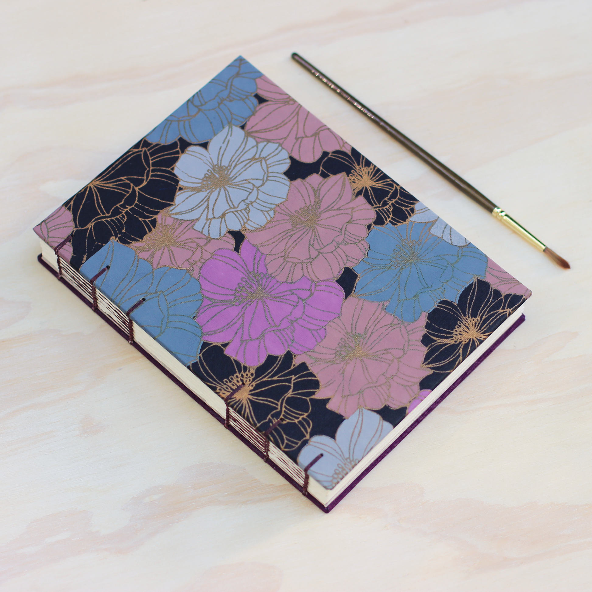 Floral arches sketchbook by Lake Michigan Book Press next to a paintbrush on a light wooden surface