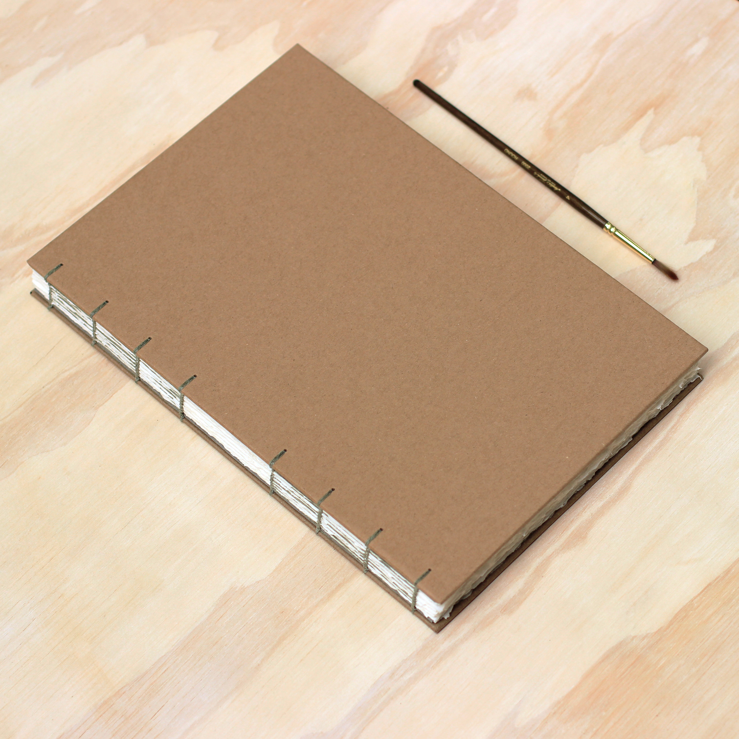 Kraft watercolor arches sketchbook with a paintbrush on a wooden surface