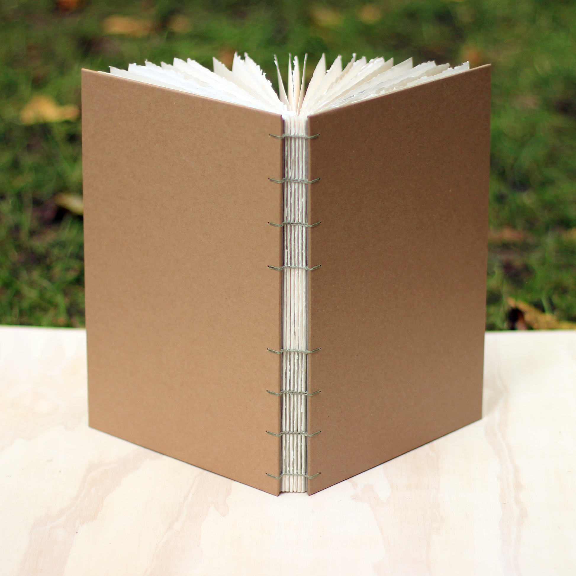 kraft sketchbook with ladder binding on a wood surface with a green grass background