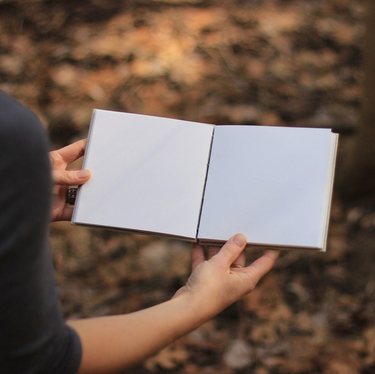 Person holding an open notebook in a natural setting with blurred background