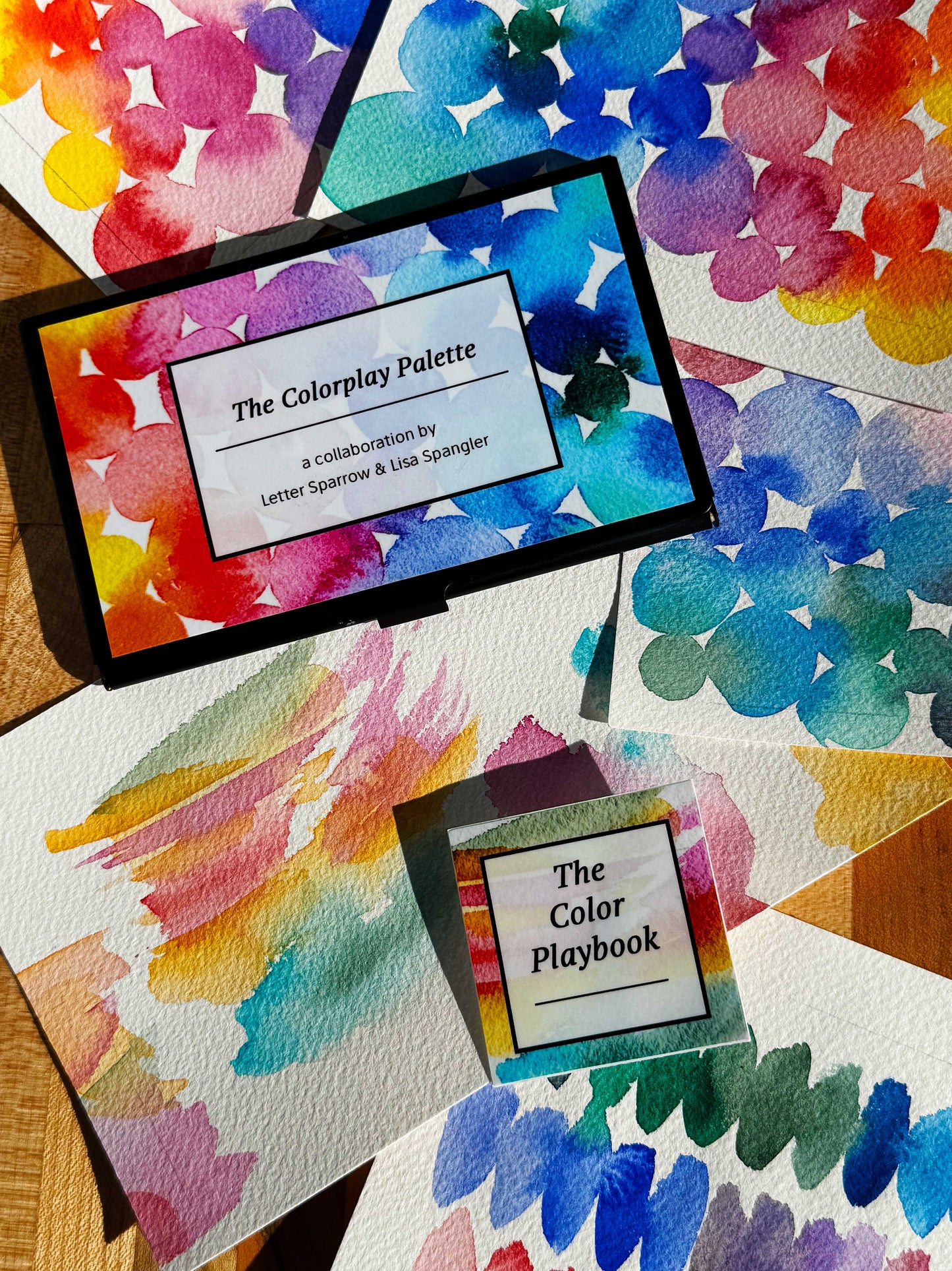 Colorful watercolor swatches with 'The Colorplay Palette' and 'The Color Playbook' on a wooden surface.