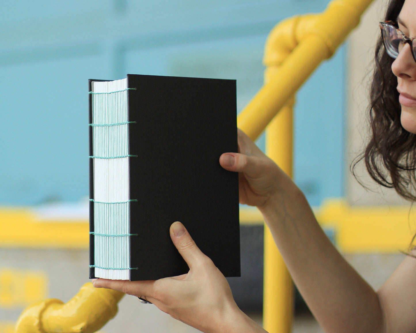 hands holding gray fat watercolor sketchbook with green binding thread