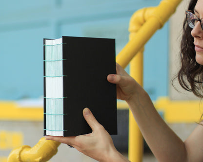 hands holding gray fat watercolor sketchbook with green binding thread