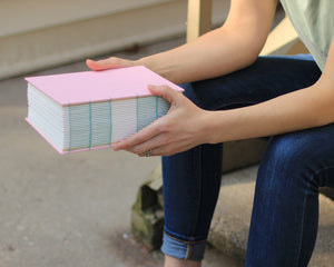 hands holding very 365 page pink sketchbook filled with watercolor paper