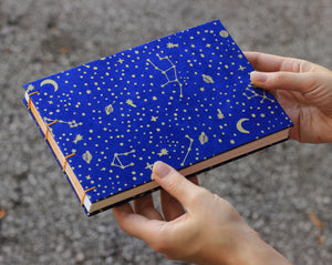 hands holding blue watercolor sketchbook with moon, stars and planets