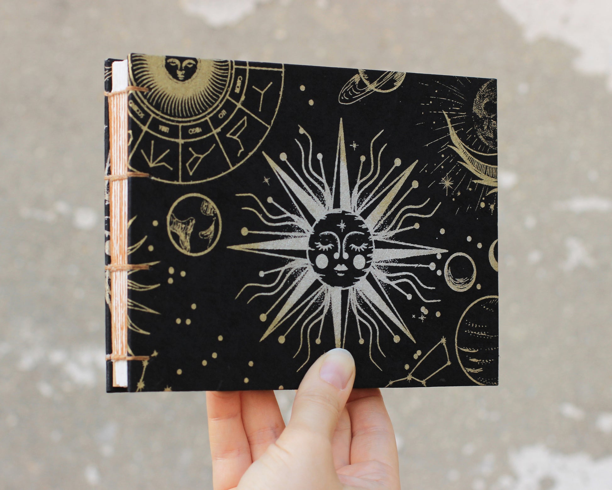 black sketchbook with silver sun on cover held by hand on gray background