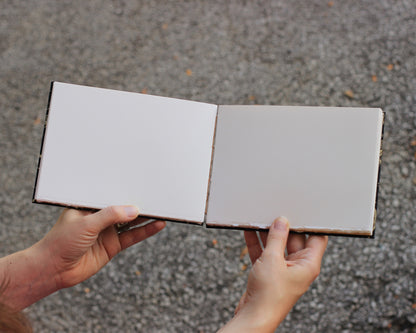 blank sketchbook held open by two hands against gravel background