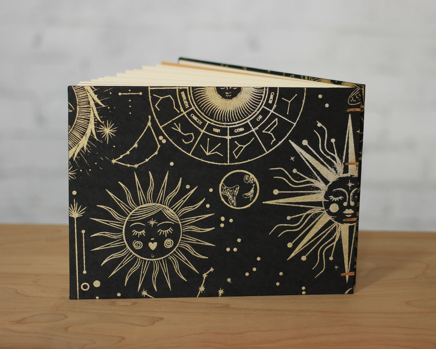 black sketchbook with gold suns with faces sitting on wood surface with white background