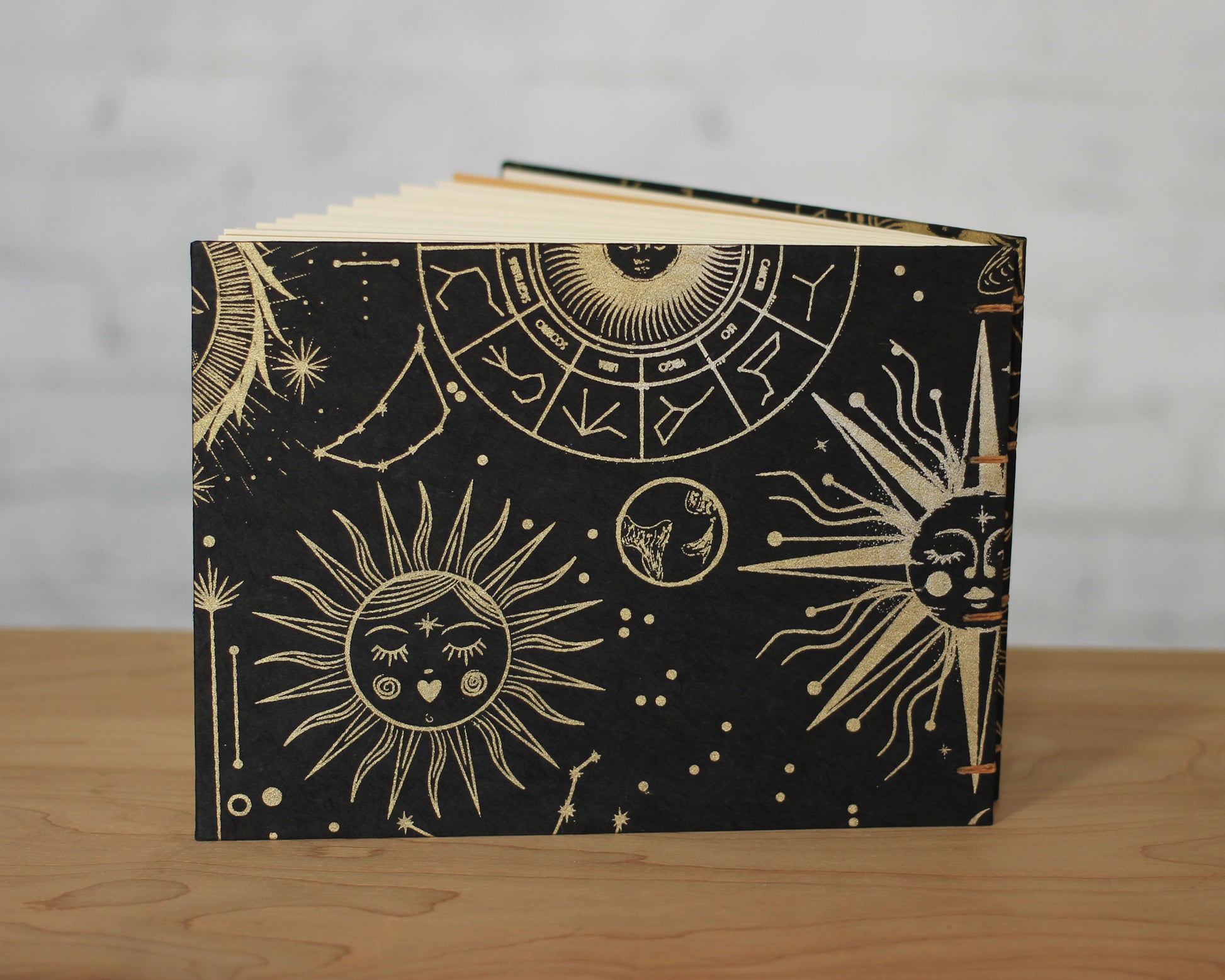 black sketchbook with gold suns with faces sitting on wood surface with white background
