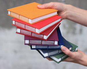 hands holding sketchbooks in gray, green, purple, blue, red, orange and yellow